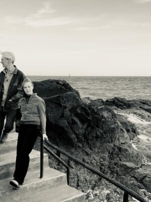 Black & white photo of Kelsey with her backing band posing on concrete steps next to a rugged sea.