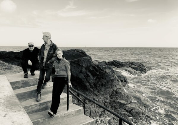 Black & white photo of Kelsey with her backing band posing on concrete steps next to a rugged sea.