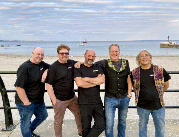 The Countrymen standing in front of a beach and blue sky.