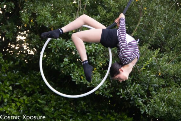 A circus performer hangs in the air, hunched backwards over a hula hoop.