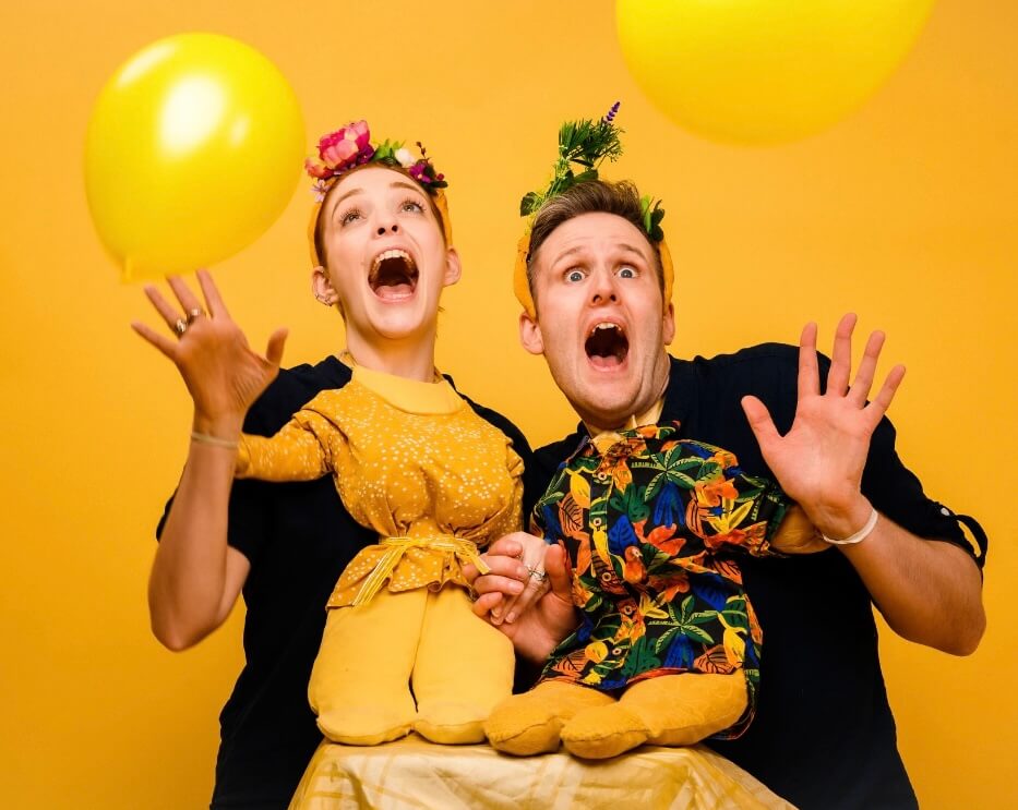 Titania and Oberon look surprised as two yellow balloons float in the foreround.