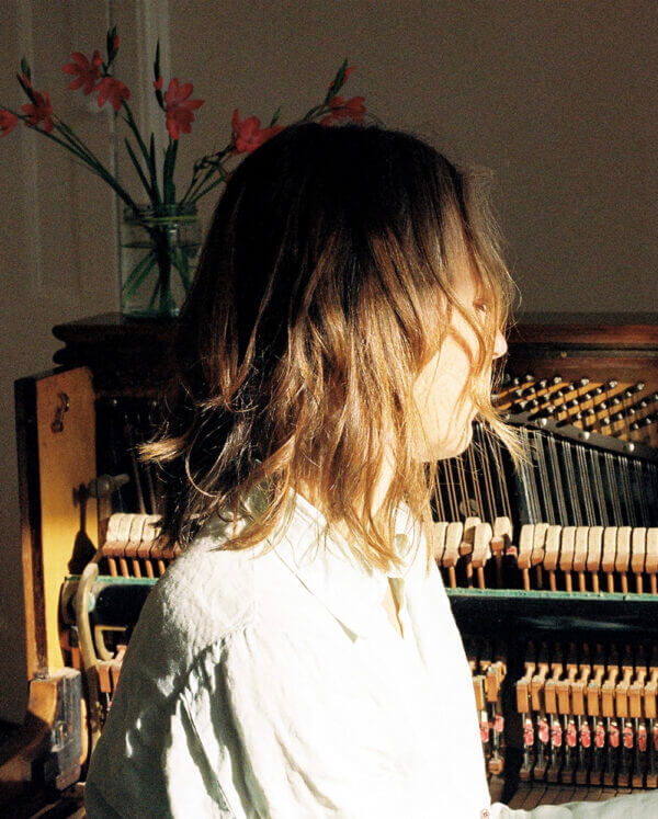 A lady sits side on to the camera in front of an open, upright piano.