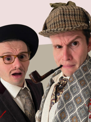 Holmes and Watson dressed in classic Sherlock attire, stare down the camera.