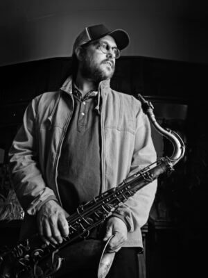 Black and white image of Pete Truin holding his saxophone and gazing off to the side