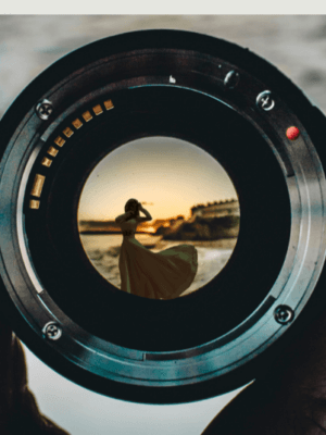 A hand holding up a camera lens. A silhouetted figure dances inside the lens.